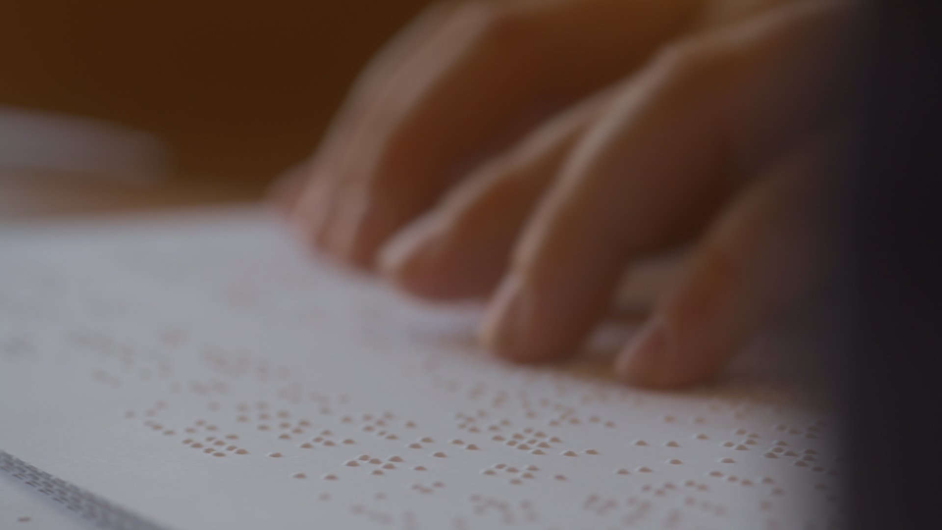 A person's fingers read a page of Braille text by gently touching the raised dots on the paper.