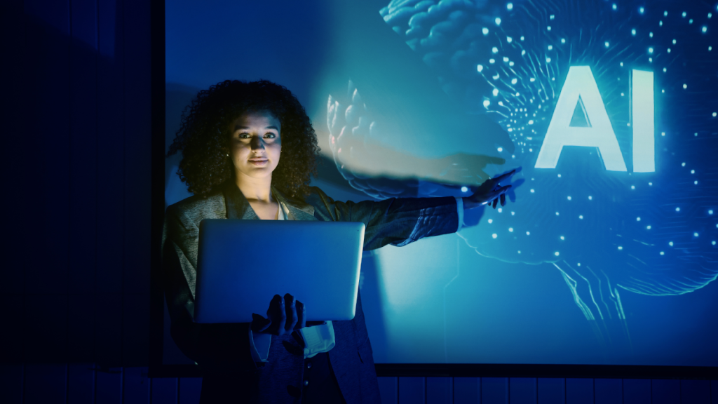 A person holding a laptop stands in front of a screen displaying the letters "AI" and a digital graphic, pointing towards the projection.