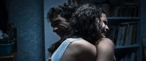 Two people with wet hair embrace tightly in a dimly lit room, with shelves of books visible in the background.