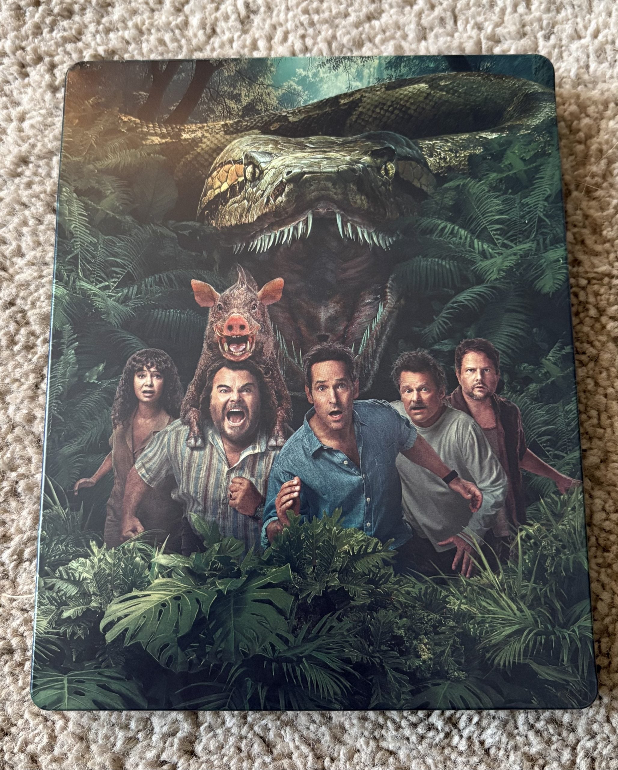 Five people and a pig stand in a jungle with a large snake looming behind them, surrounded by dense green foliage.