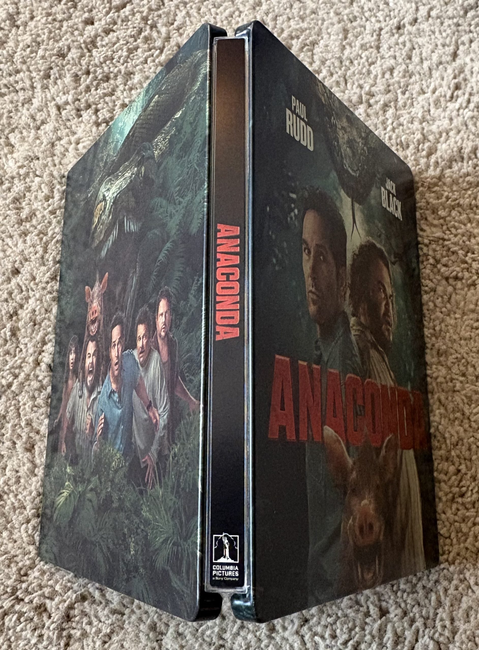 A Blu-ray case for the movie "Anaconda" is shown standing upright, featuring actors Paul Rudd and Jack Black on the cover amid a jungle background.