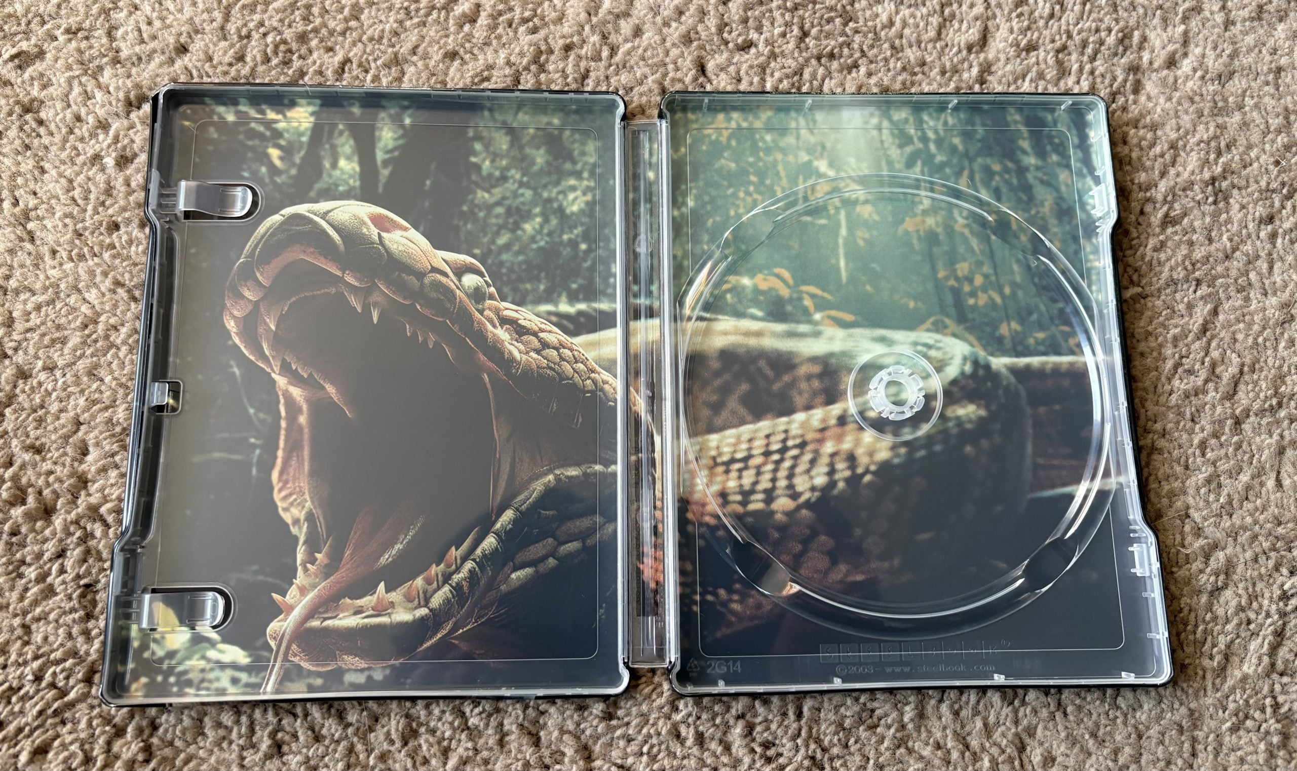 Open empty DVD case with an image of a large snake with its mouth open printed on the inside cover, lying on a carpeted surface.