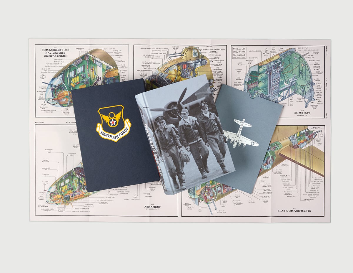 A U.S. Air Force folder, a black-and-white photo book of airmen, and a blue book with an airplane graphic are placed on top of a technical diagram of a bomber aircraft.