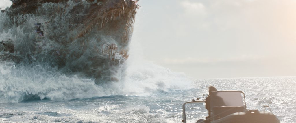 A person in a small boat faces a large, rocky cliff as ocean waves crash against it under a cloudy sky.