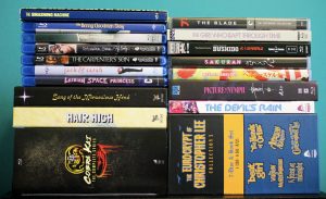 A collection of assorted Blu-ray and DVD cases arranged in two stacks against a turquoise background.