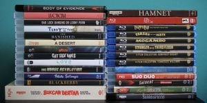 No Streaming Required: Physical Media Spotlight For The Week Of March 3rd A collection of DVD and Blu-ray movie cases stacked in two columns against a blue background, with various film titles visible on the spines.