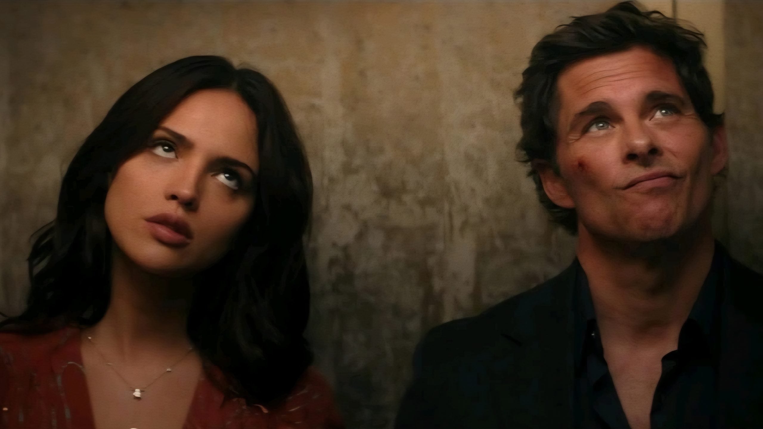 Two people stand side by side against a plain wall, both looking upward with unimpressed or exasperated expressions.