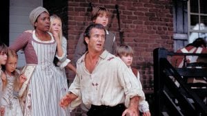 Sony To Release ‘The Patriot’ On 4K UHD Blu-Ray SteelBook With Two Cuts Of The Film This June A man with a blood-stained shirt stands protectively in front of children and a woman dressed in historical clothing outside a brick building.