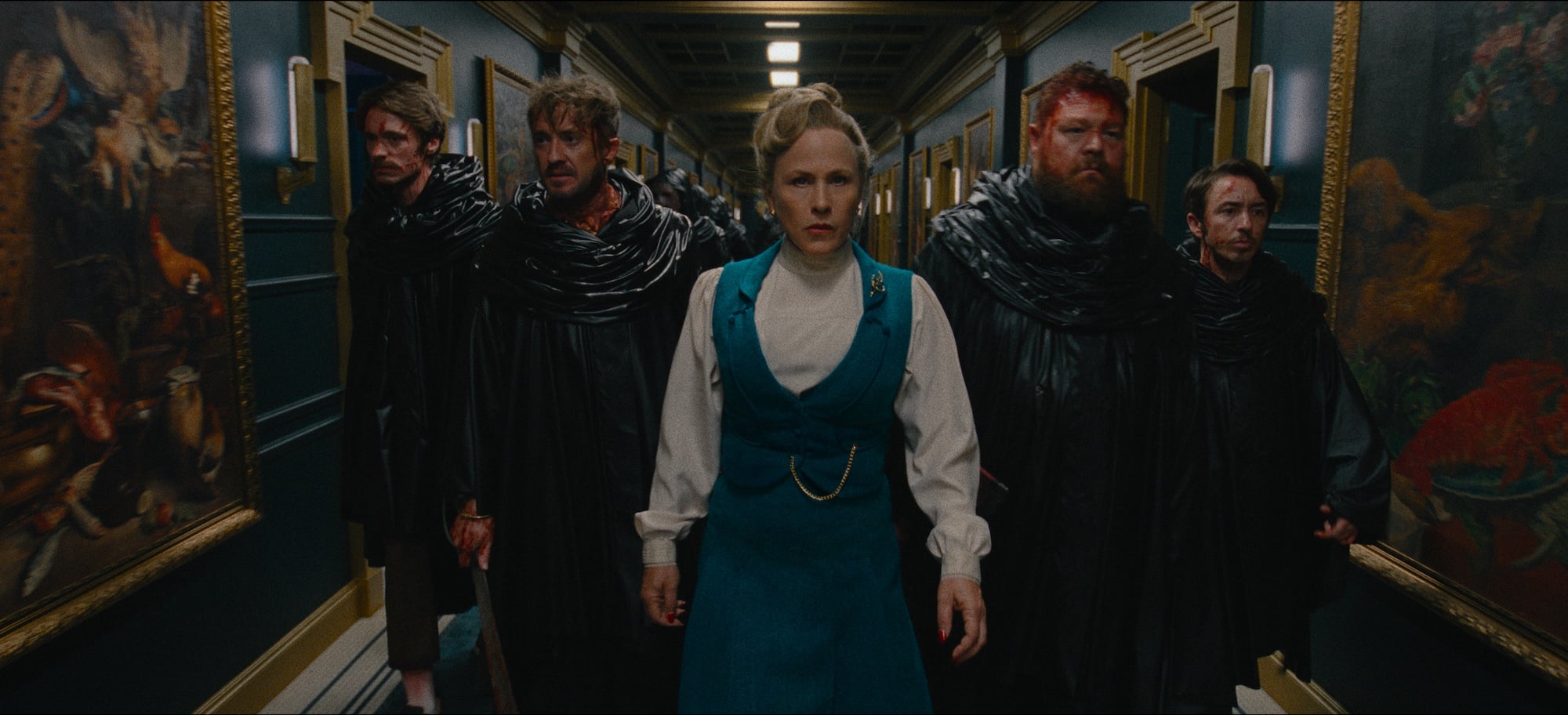 A woman in a blue dress leads four men in black cloaks down a hallway lined with paintings. All have serious expressions.