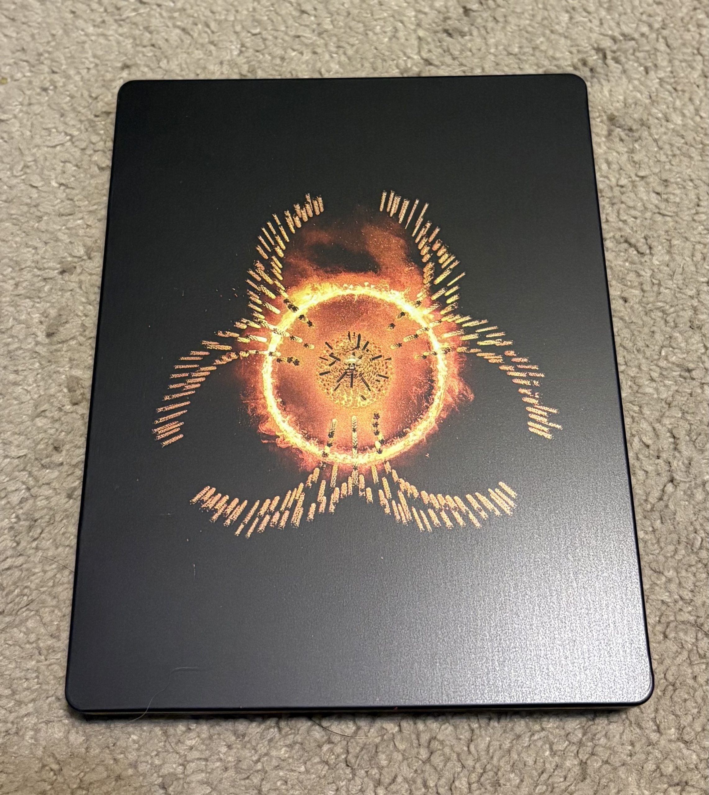 A black metal case featuring an orange and yellow fiery circular symbol in the center, resting on a beige carpeted floor.
