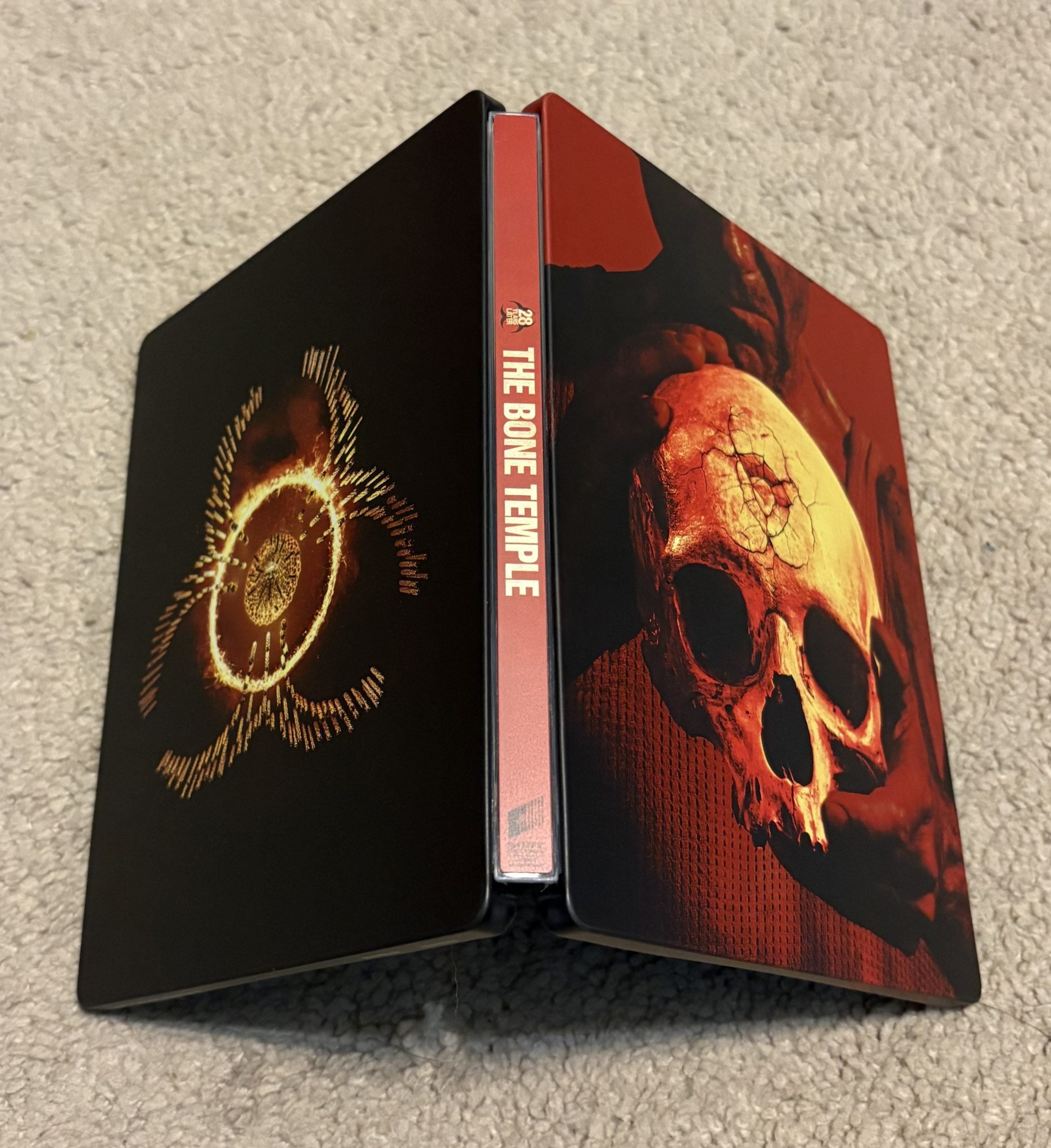 A steelbook case titled "The Bone Temple" standing open on a carpet, featuring a skull and a circular symbol on the covers.