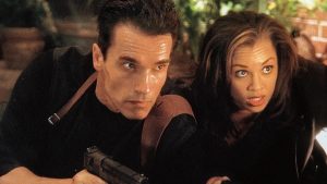 Two people crouch together in a tense moment, one holding a handgun, both looking intently in the same direction.