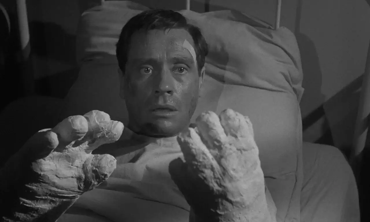 A man lies in a hospital bed looking distressed, with both hands and wrists covered in thick plaster casts.