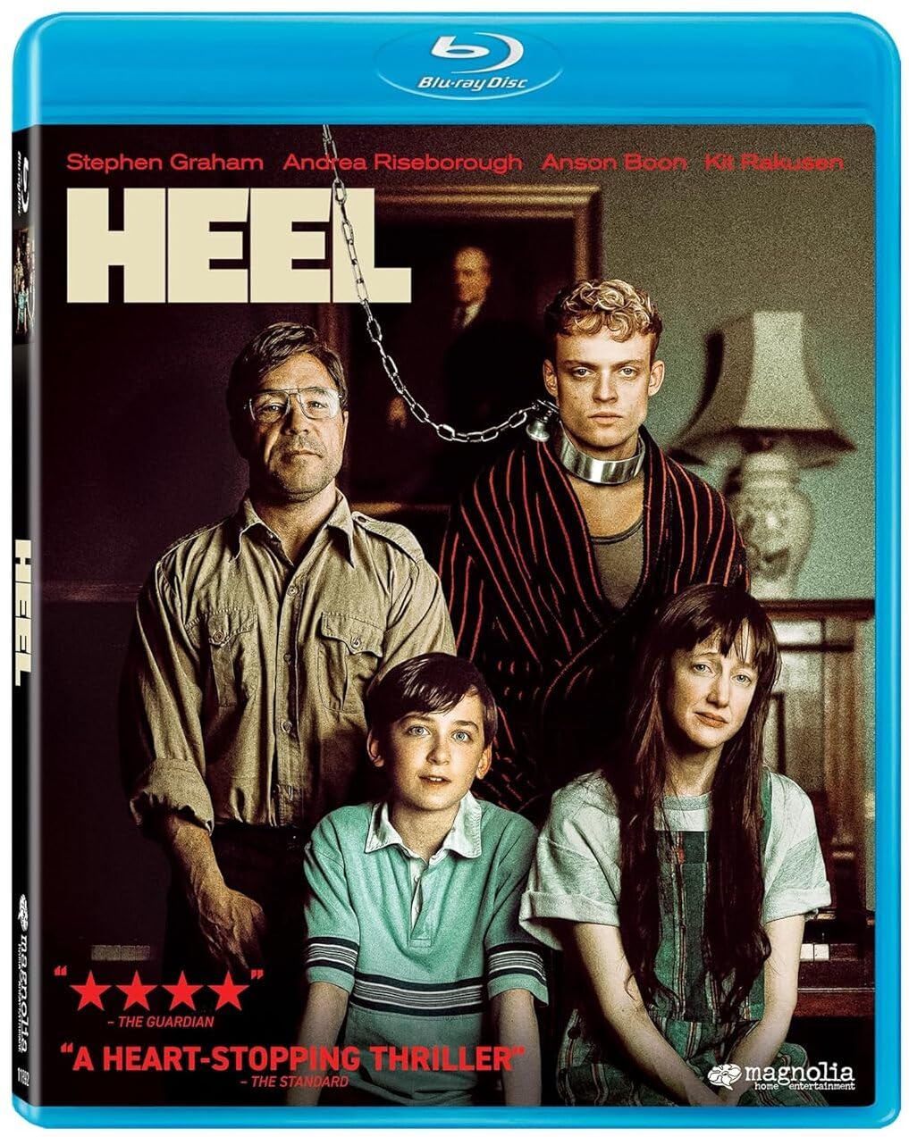 Blu-ray cover for the film "Heel" showing four people posed in a living room; one man is on a leash held by another man who stands behind him, with a woman and a boy seated in front.