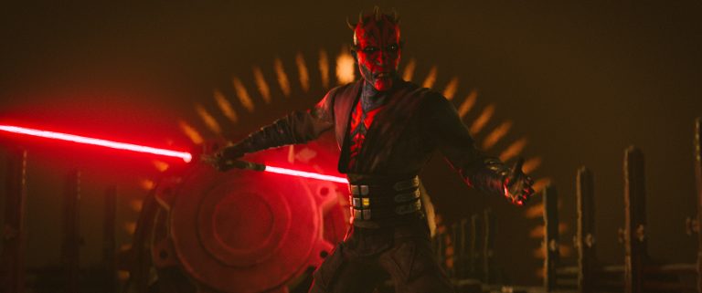 A character with red and black facial markings wields a double-bladed red lightsaber in a dim, industrial setting with a circular mechanical structure behind them.