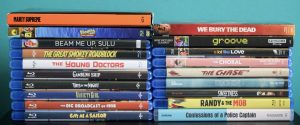 A collection of DVD and Blu-ray cases stacked vertically in two columns, displaying various movie and TV titles against a teal background.