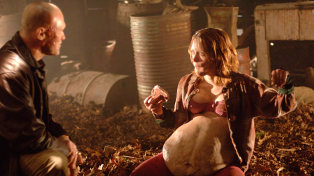 ‘Slither’ 4K UHD Blu-Ray SteelBook Review – A Properly Disgusting Creature Feature From James Gunn A woman with a large, round belly and a man with a beard in a dimly lit, rustic setting.