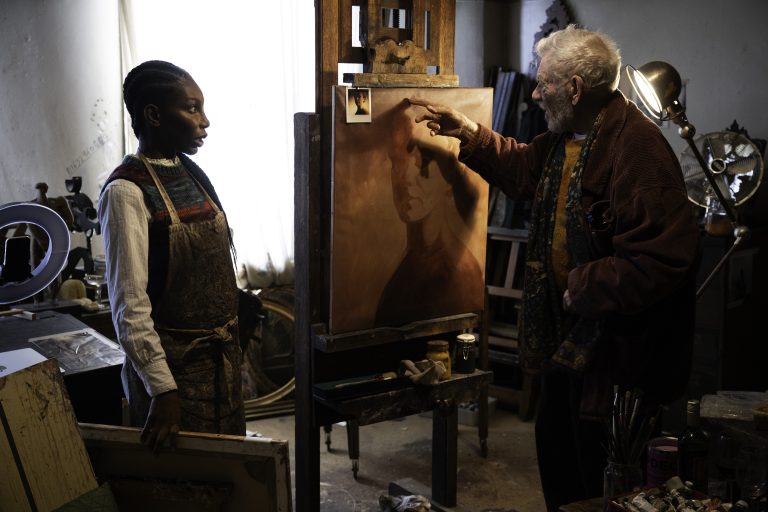 Two artists working on a portrait in an art studio with painting supplies and artwork.