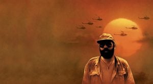 A man in military attire stands in front of a large orange sun, with several helicopters flying in the sky behind him.
