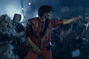 Lionsgate To Release The Box Office Smash Biopic ‘Michael’ On 4K UHD Blu-Ray A man in a red jacket dances with a group of people dressed as zombies in a dark, foggy outdoor setting.