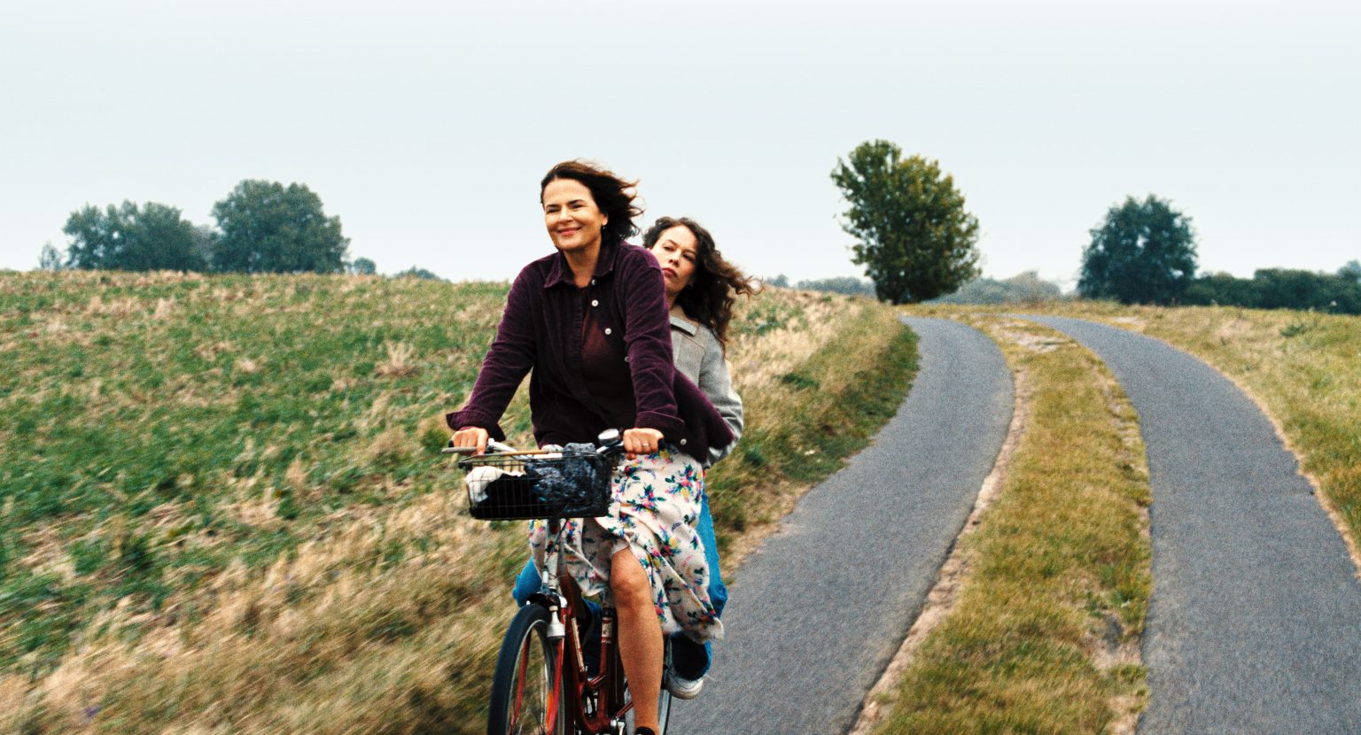 Women cycling outdoors on a rural path with greenery and trees in the background.