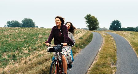 Women cycling outdoors on a rural path with greenery and trees in the background.