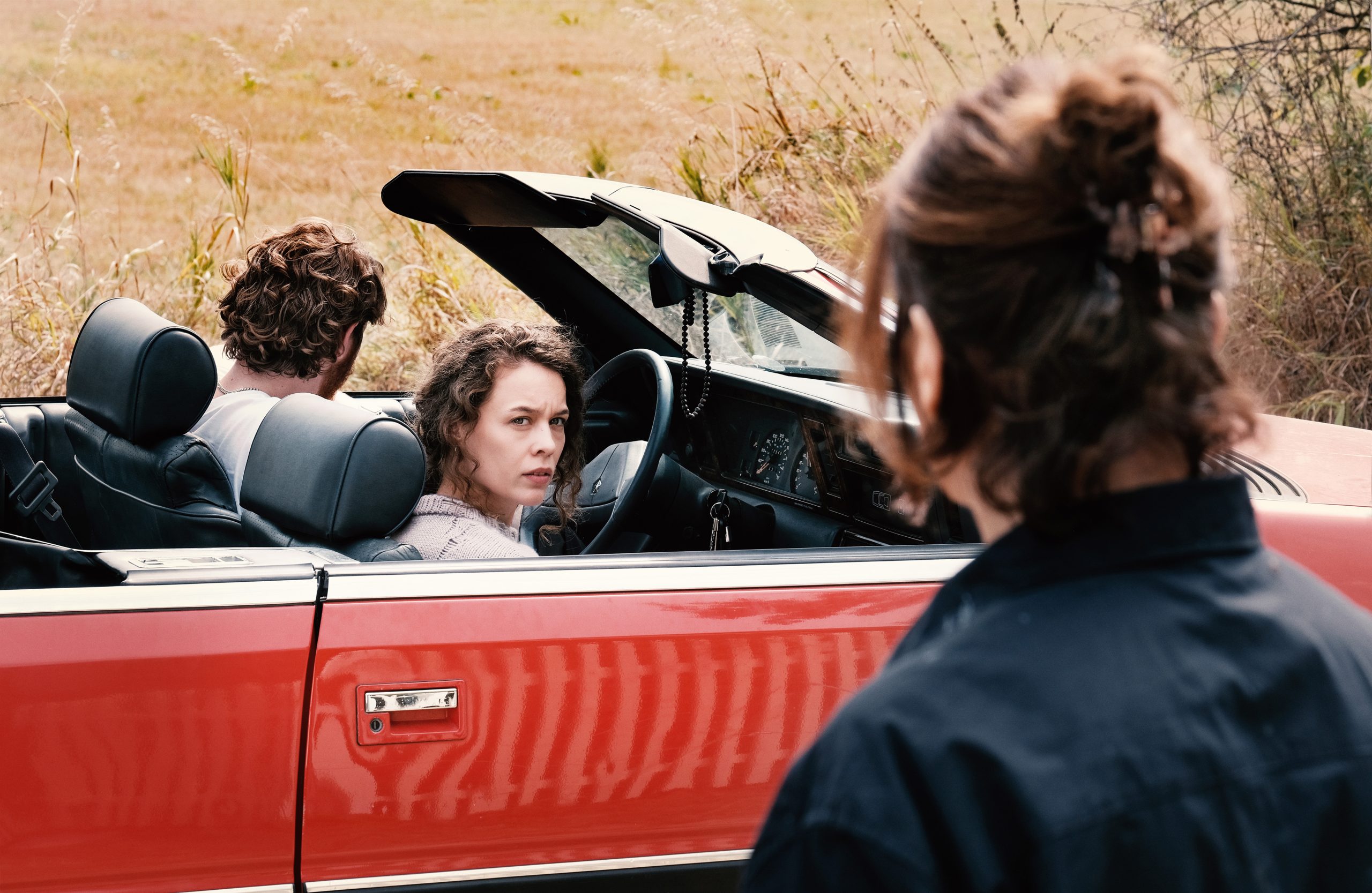 Escape scene with two women in a red convertible car in a rural area.