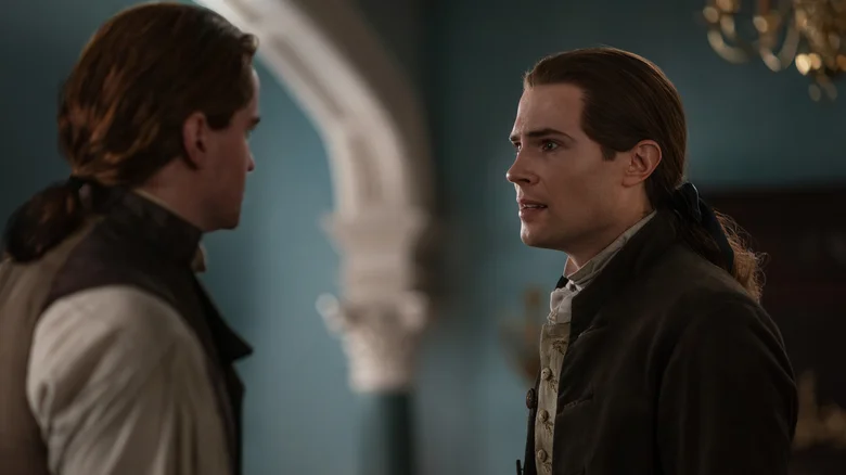 Two men in historical clothing face each other indoors, appearing to have a serious conversation.