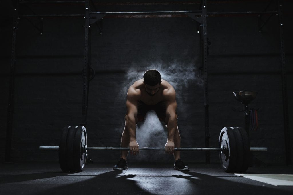 A person prepares to lift a barbell in a gym, with chalk dust in the air and gym equipment in the background.