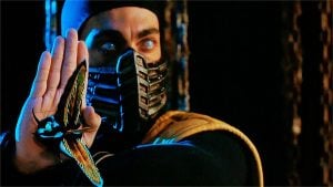A person in a black and yellow costume with a masked face extends a hand, from which a mechanical creature emerges, set against a dark background.