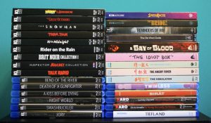 A collection of DVD and Blu-ray cases arranged vertically in two rows against a teal background, featuring film and series titles in various genres.
