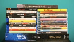 No Streaming Required: Physical Media Spotlight For The Week Of May 26th A collection of assorted DVD and Blu-ray movie cases stacked in two columns against a teal background.