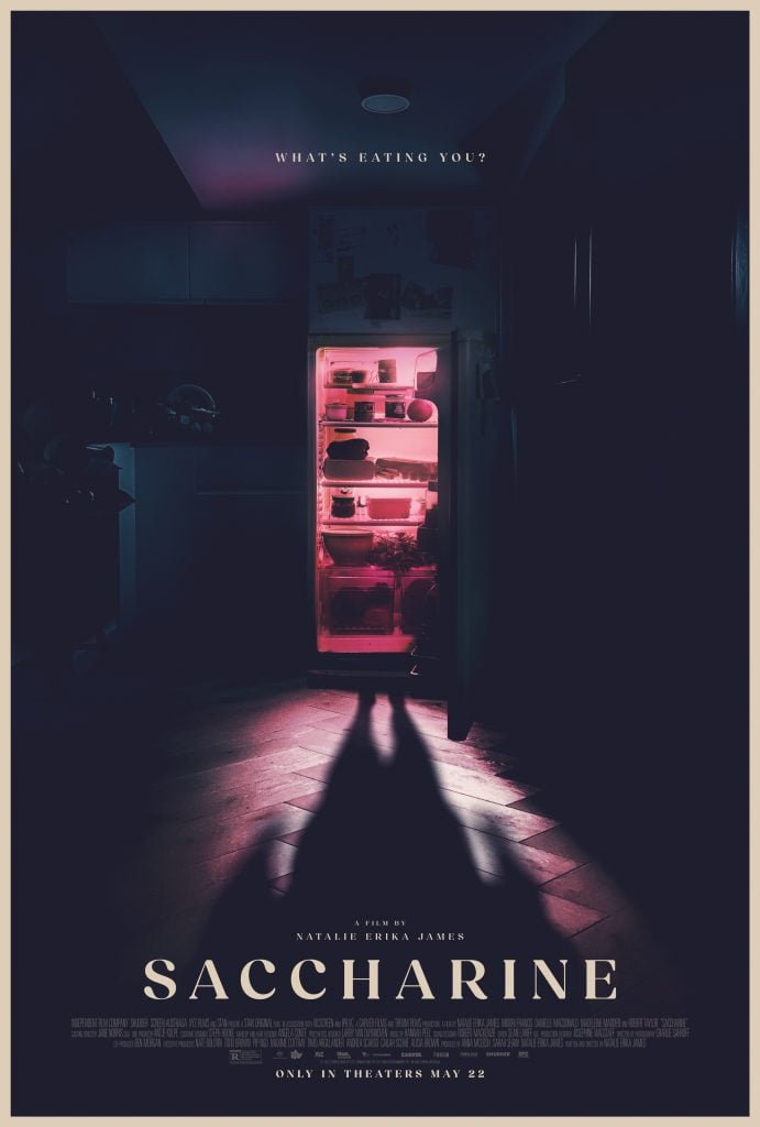 A dimly lit kitchen shows an open refrigerator glowing pink, casting long shadows of a person standing in front of it; text reads "SACCHARINE" and "What's eating you?.