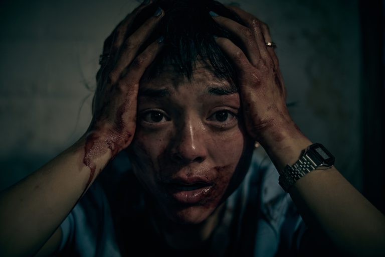 Woman distressed, holding her head with bloodstained hands, emotional distress, dark background.