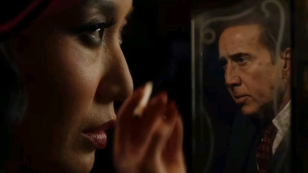 A woman’s face is seen in close-up, with the reflection of a serious-looking man visible in a mirror beside her.