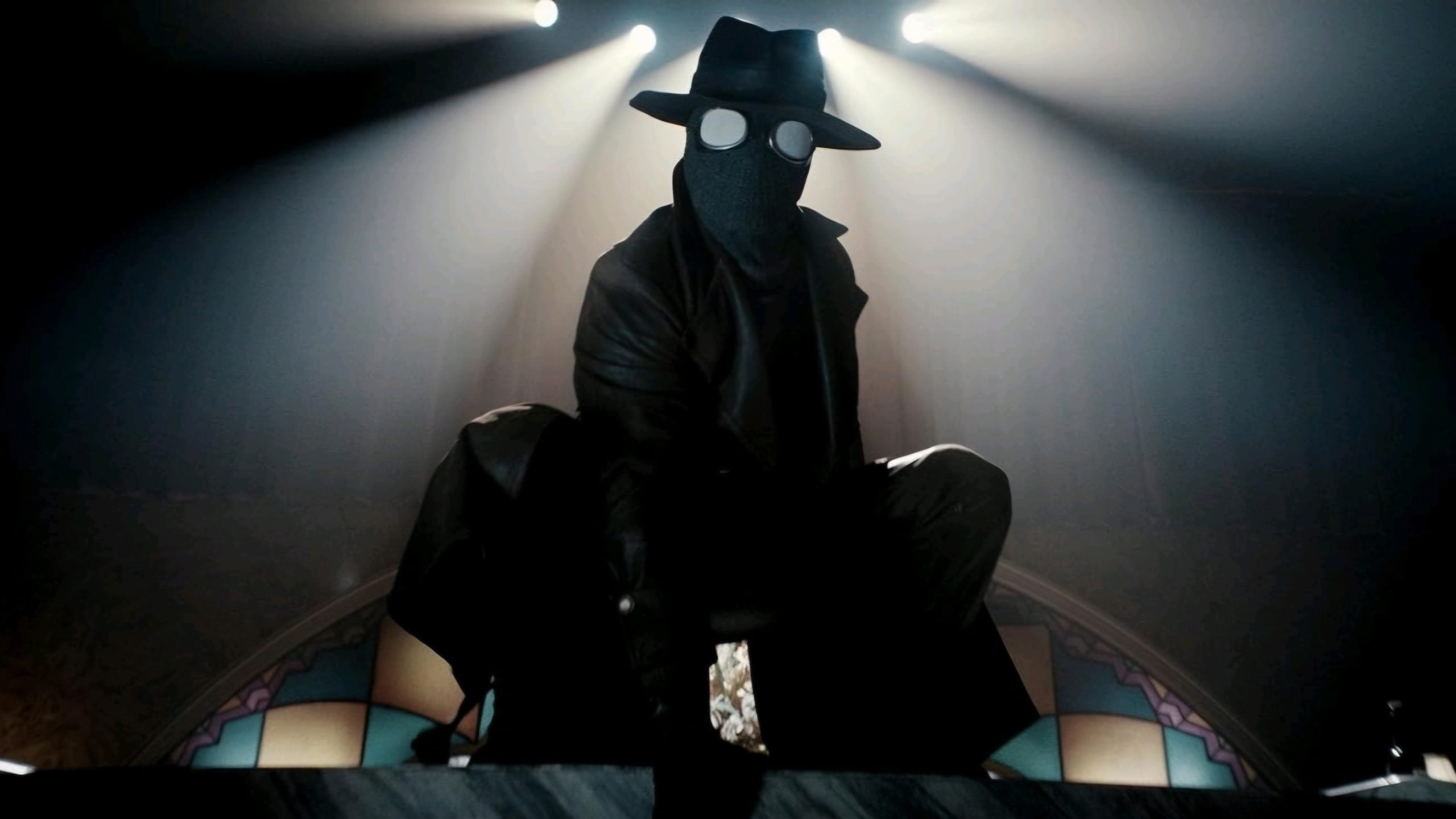 A person in a black trench coat, wide-brimmed hat, and goggles crouches on a ledge under dramatic lighting, with stained glass in the background.