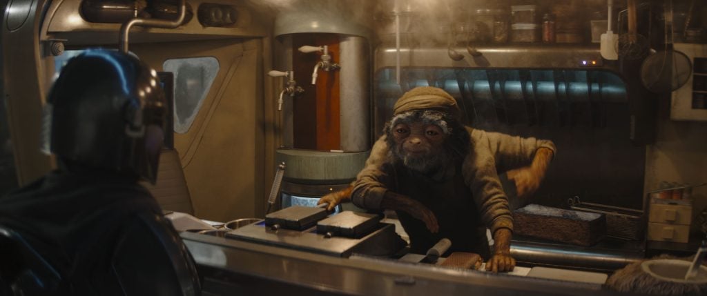 A humanoid monkey-like creature wearing a hat stands behind a counter in a futuristic kitchen, facing a person in dark armor.