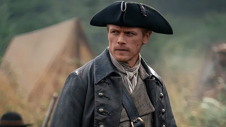 A man in historical clothing and a tricorn hat stands outdoors near a canvas tent, looking to the side with a serious expression.