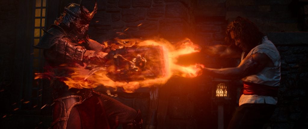 A warrior in dark armor and a man in white battle over a large, fiery, glowing object emitting flames, with stone walls and a lantern in the background.