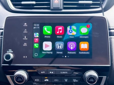 Car dashboard touchscreen displaying Apple CarPlay with app icons including Phone, Music, Maps, Messages, Now Playing, Honda, Podcasts, and Audiobooks.