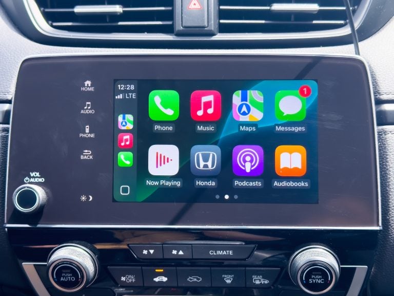 Car dashboard touchscreen displaying Apple CarPlay with app icons including Phone, Music, Maps, Messages, Now Playing, Honda, Podcasts, and Audiobooks.