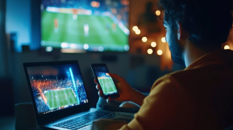 The Evolution of Sports Streaming Technology And Its Impact on Modern Broadcasting A person watches a soccer match on TV, with the same match displayed on a laptop and smartphone in a dimly lit room.
