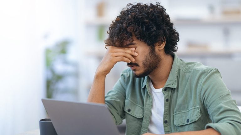 How AI Planning Reduces The Mental Load of A Busy Week A person sits at a desk with a laptop, resting their face in one hand, appearing stressed or tired.