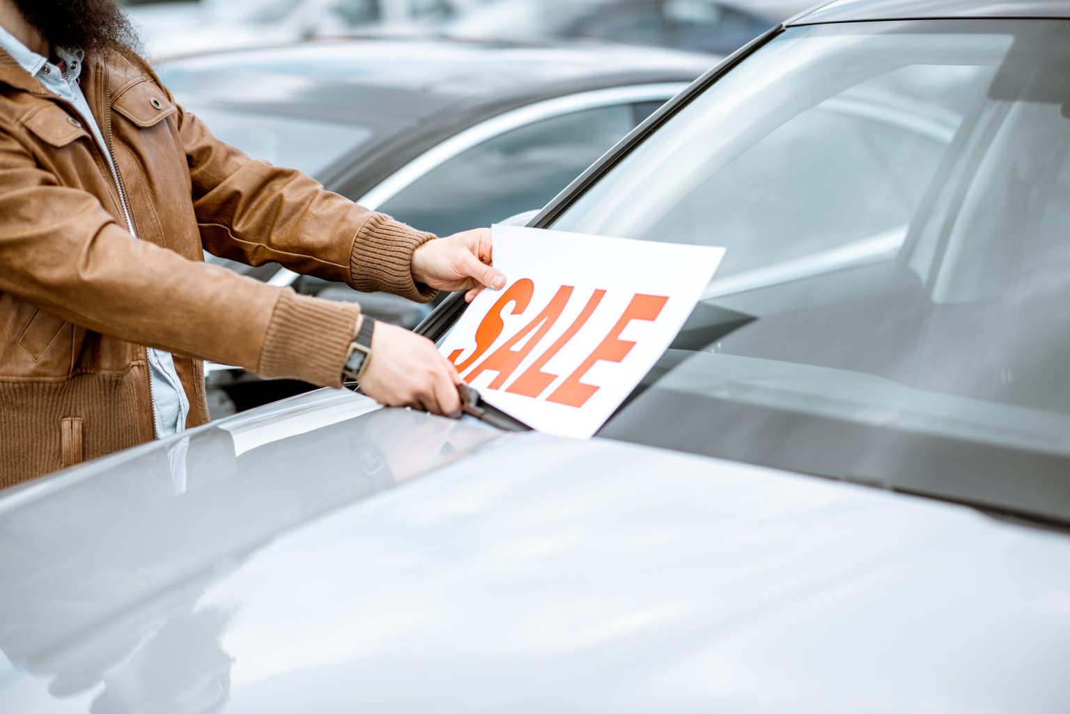 Advanced Driver Assistance Technologies Available In Modern Used Cars A person places a "SALE" sign on the windshield of a parked car in a lot.