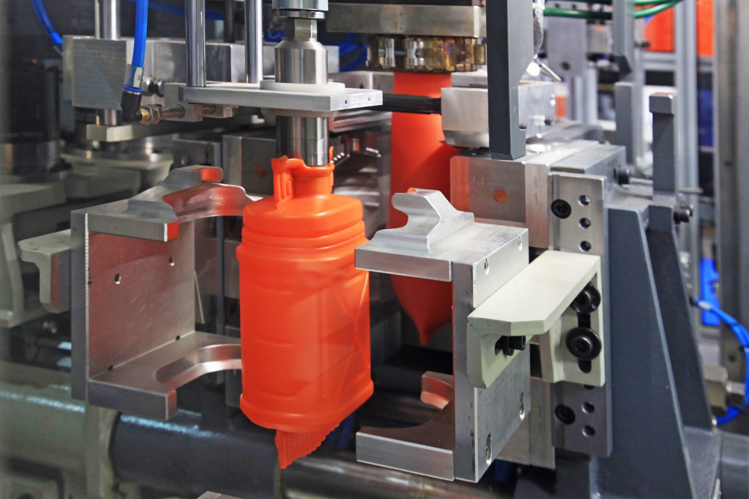 Close-up view of an orange plastic bottle being formed in an industrial blow molding machine.