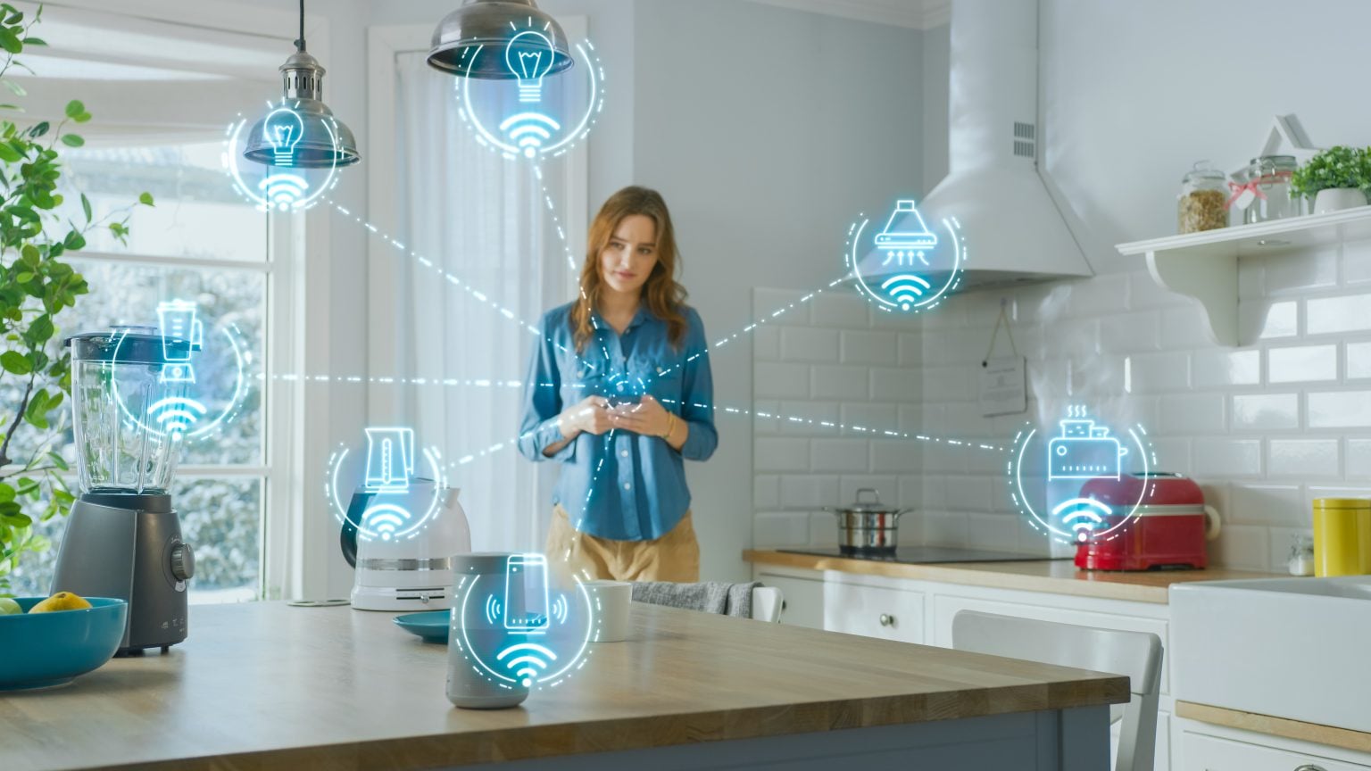 A woman stands in a modern kitchen using a smartphone, surrounded by holographic icons representing connected smart home devices and appliances.
