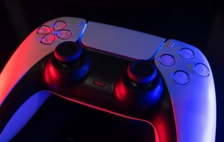 PlayStation Reveals Sony’s AI Strategy At Corporate Presentation A close-up of a white video game controller lit with red and blue lights against a dark background.