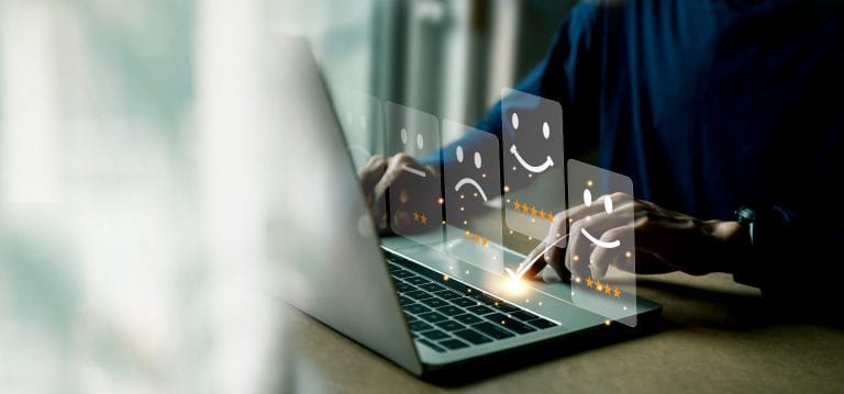 Person using a laptop with floating digital icons showing various satisfaction ratings, including happy, neutral, and sad faces with star ratings.