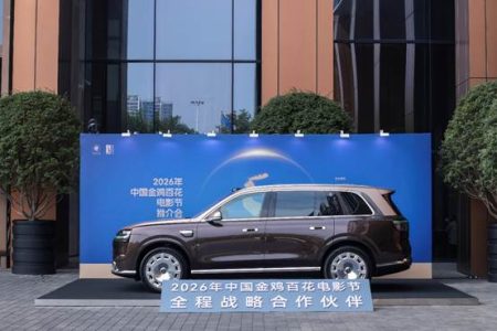 A brown SUV is displayed in front of a blue backdrop with Chinese text, outside a modern building, promoting the 2026 China Golden Rooster and Hundred Flowers Film Festival.