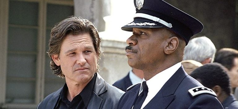 Two men stand side by side outdoors; one wears a black jacket, the other is in a police uniform with a hat.